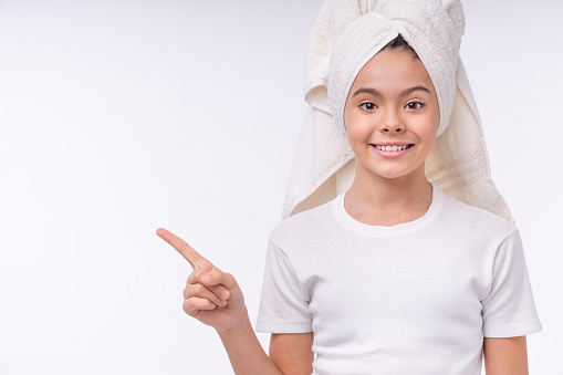 Beautiful little teen girl in spa towel pointing at copy space isolated over white background