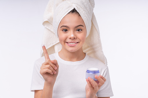 Happy cheerful teenage girl in spa towel using face cream isolated over white background