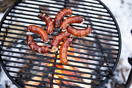 Fresh sausages grilling over the bonfire shot from above.\nShot with Canon R5