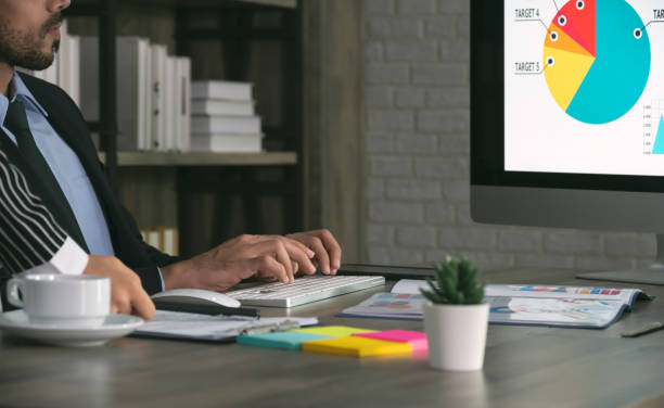 istock Two business colleagues working in office and using computer. Man sitting at his desk with female colleague standing besides him 1303486072