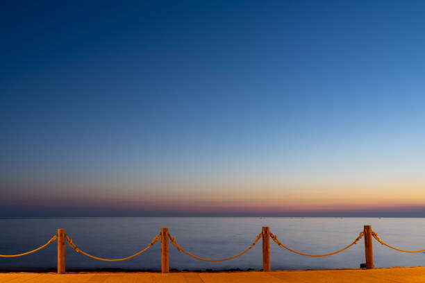 beachfront sidewalk illuminated by street lights and a calm ocean sunset behind with copy space