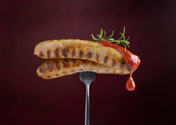 grilled sausages with tomato sauce and rosemary on fork on dark burgundy background. red sauce dripping from sausages. close-up. - sausage bratwurst barbecue grill barbecue imagens e fotografias de stock