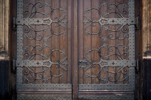 Metal ornaments and hinges on two brown wooden church doors.