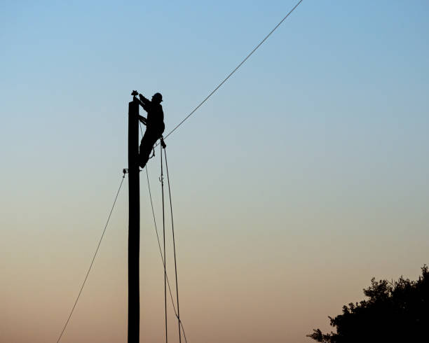 Lineman at Sunset A lineman installs electric wire on a rural utility pole at sunset telephone pole stock pictures, royalty-free photos & images