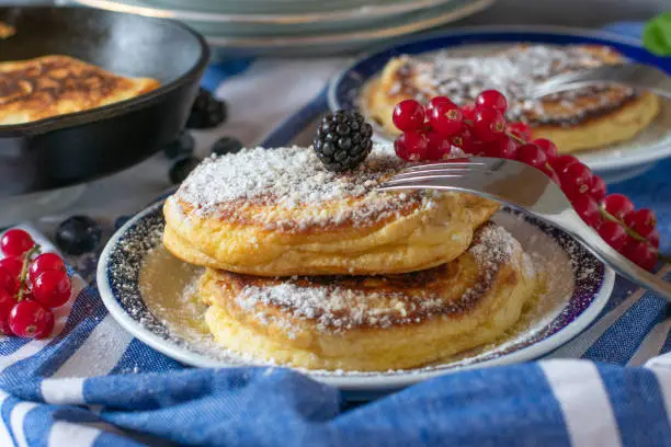 fresh baked breakfast pancakes with melted butter, berries and powdered sugar served on plates