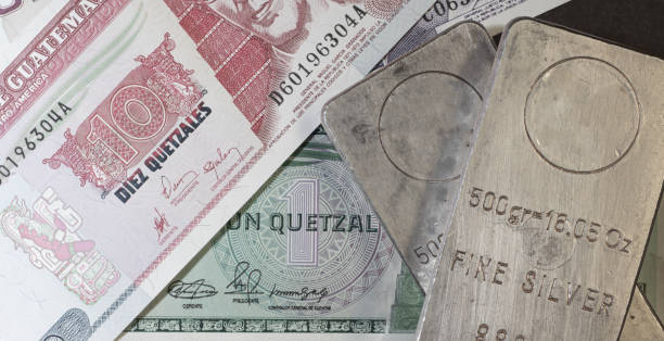 istock Two silver bars lie on Quetzal banknotes. 1303497934