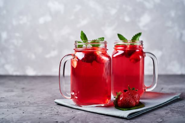 Homemade strawberry lemonade with mint in mason jar on gray concrete table background, copy space. Cold summer berry drink in sparkling glasses. Fresh vitamin beverage stock photo