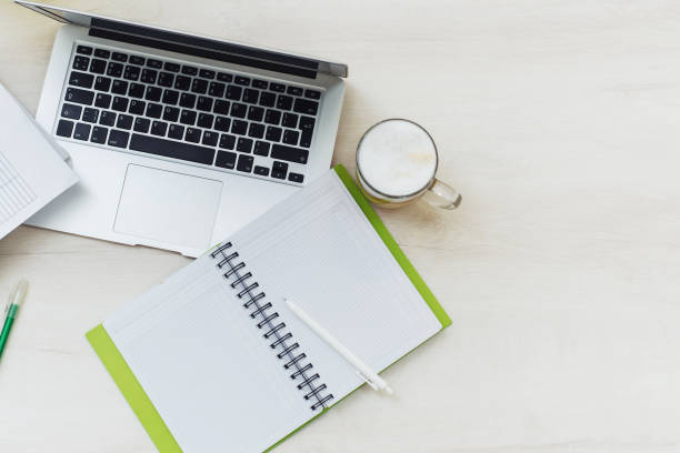 istock Top view office desk with laptop, notebooks and coffee cup on white color background. Office table with blank notebook and laptop 1303499723