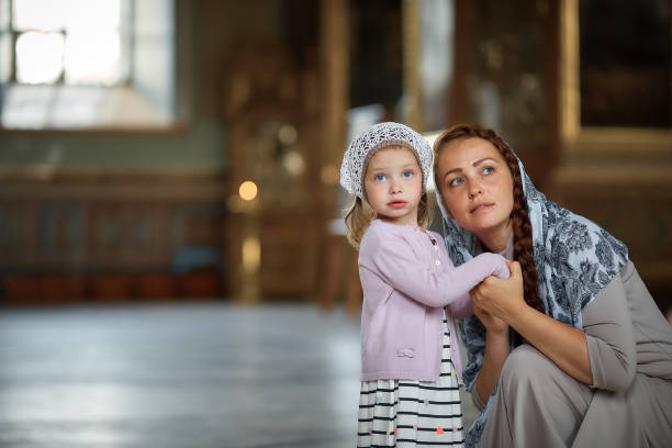 Young mother and her little blond Caucasian daughter with candles in Orthodox Russian Church stock photo