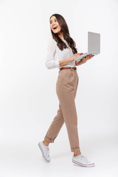 Full length portrait of a happy asian businesswoman Full length portrait of a happy asian businesswoman holding laptop computer and looking away isolated over white background whole stock pictures, royalty-free photos & images