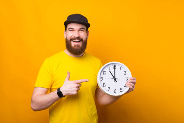istock Charming happy smiling bearded hipster man pointing at big white watch 1303502597