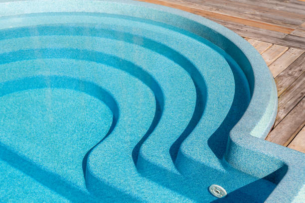 New modern fiberglass plastic swimming pool entrance step with clean fresh refreshing blue water on bright hot summer day at yard or resort hotel spa area. Wooden flooring deck of teak or larch board. nuevo paso de entrada moderna a la piscina de plástico de fibra de vidrio con agua azul fresca y refrescante limpia en el caluroso día de verano en el patio o en la zona de spa del hotel resort. cubierta de suelo de madera de teca o tabla de alargamiento