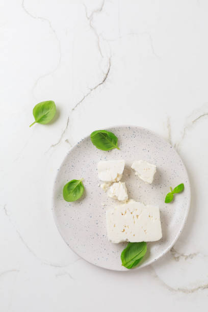 Feta cheese with basil leaves on plate and white background Feta cheese with basil leaves on plate and white background. feta cheese block stock pictures, royalty-free photos & images