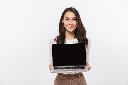 Portrait of a smiling asian businesswoman showing blank screen laptop computer isolated over white background