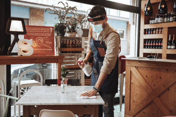 istock Waiter wearing protective face mask and face shield disinfecting tables in the restaurant 1303509139