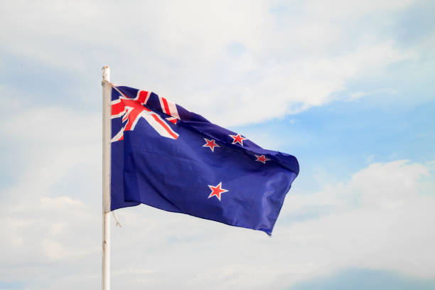 istock New Zealand flag on a blue sky with clouds background 1303510220