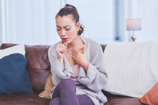 I'm coming down with something Cropped shot of an attractive young woman sitting alone on her sofa at home and coughing chronic illness stock pictures, royalty-free photos & images