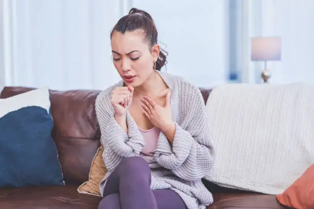 Cropped shot of an attractive young woman sitting alone on her sofa at home and coughing