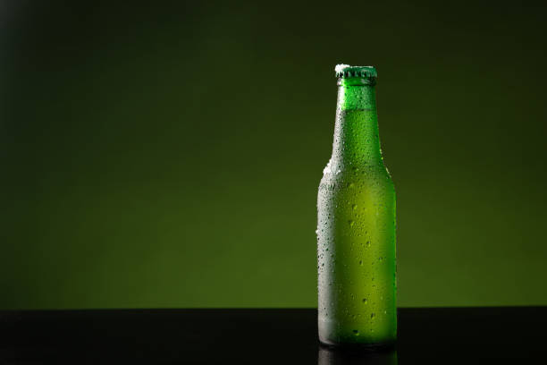 istock Bottle of cold beer with water drop on green background with copyspace. 1303511585