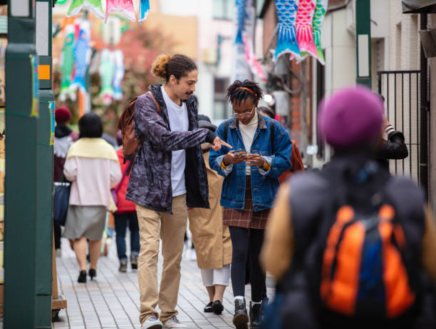 istock Two Tourists Checking a Phone While Walking the Sidewalk in Tokyo, Japan 1303514062