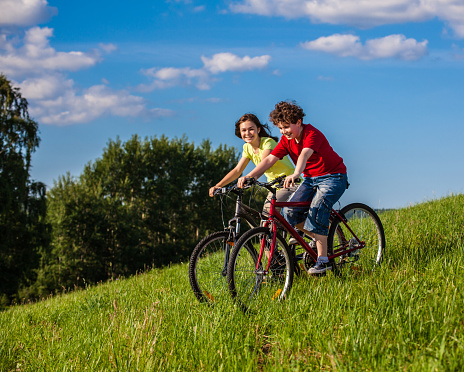 Girl and boy riding bikes against blue sky