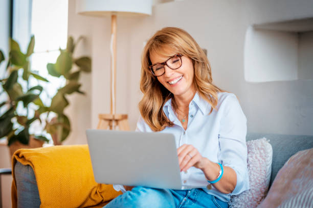 istock Happy mature woman using laptop while sitting on the couch at home 1303515231