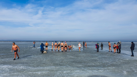 Rewa, Poland - February 22, 2021: Winter swimming. People winter bathing in the sea. A large group of people is walking on frozen water.