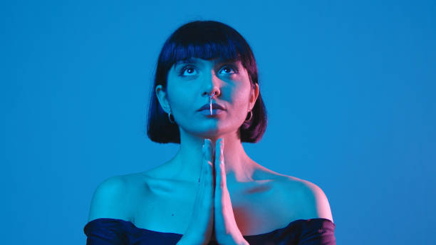 istock Young woman pray isolated on blue neon copyspace 1303517294
