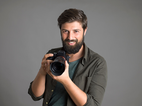 Portrait of a photographer using a digital SLR camera over gray background