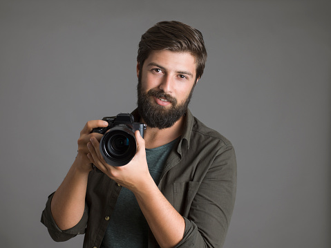 Portrait of a photographer using a digital SLR camera over gray background