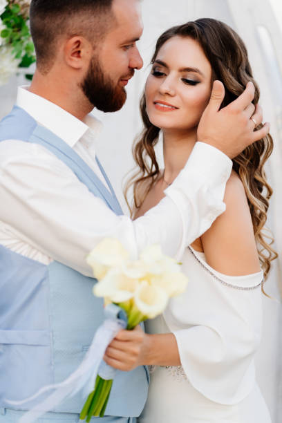 bride with long curls in a white elegant dress with beautiful bride with long curls in a white elegant dress and the groom in the blue suit. wedding ceremony in nature. two calla lillies stock pictures, royalty-free photos & images