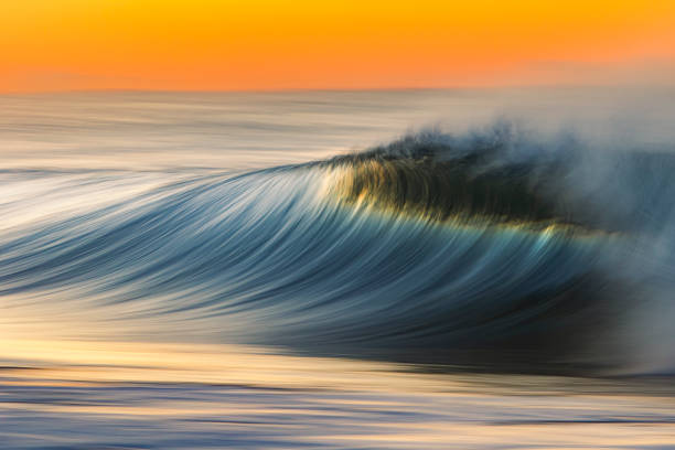 istock Smooth blue wave breaking on the beach with golden sunrise 1303522867