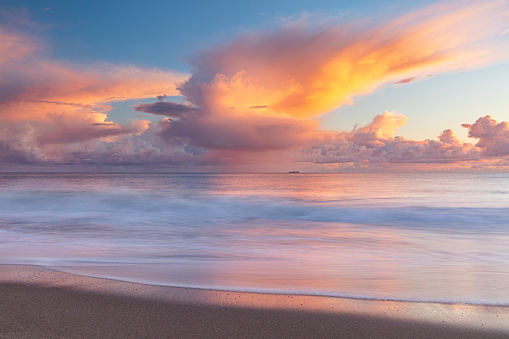 Seascape of warm pink storm cloud at sunset over the oceans shore, photographed with motion blur in California.