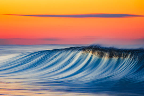 istock Smooth blue wave breaking on the beach with golden sunrise 1303528027