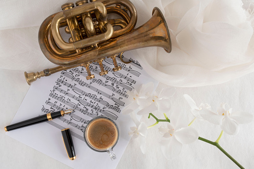 Black coffee cup on a music score with trumpet and flower