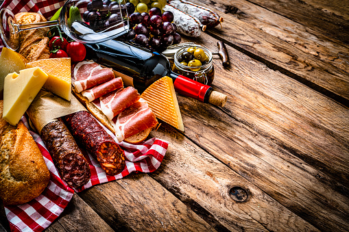 Mediterranean food: Arrangement of Iberico ham sandwich, cheeses, Spanish chorizo, bread, olives, grape and red wine on rustic wooden table. The composition is at the left of an horizontal frame leaving useful copy space for text and/or logo at the right. High resolution 42Mp studio digital capture taken with SONY A7rII and Zeiss Batis 40mm F2.0 CF lens
