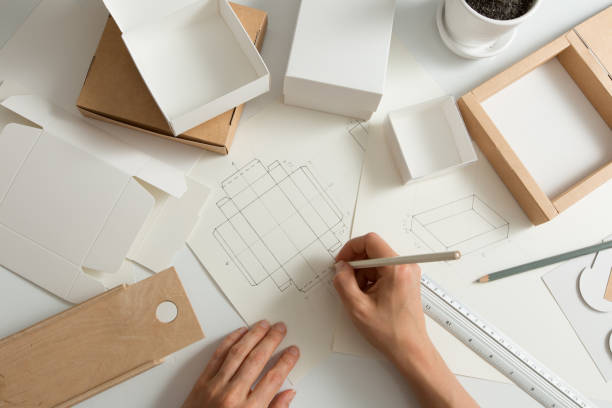 istock Designer draws a mockup for crafting cardboard box. Development of packaging design sketch. 1303532680
