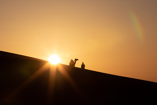 Silhouette of a nomad man with his camel in sand dunes at sunset. Liwa desert, Abu Dhabi, UAE.