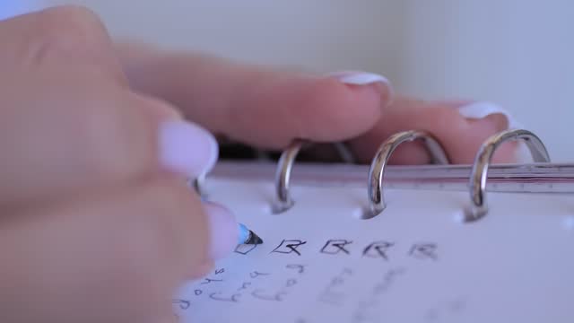 Woman putting mark on check boxes of to do list in notebook - close up