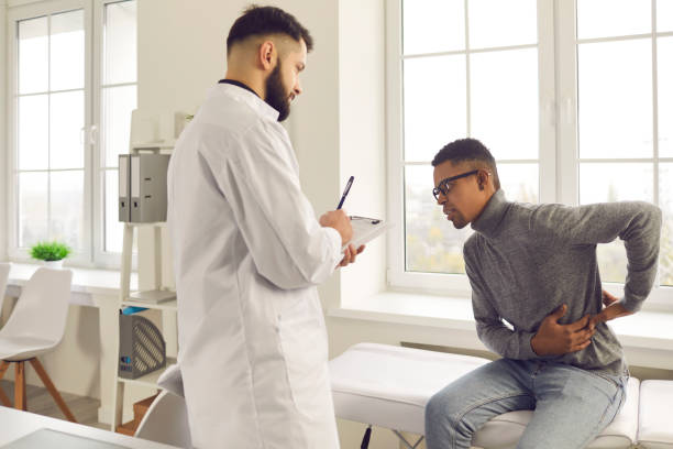 Young African-American patient telling doctor about his backache during visit to hospital stock photo