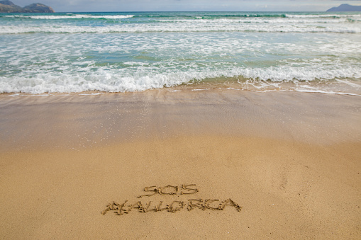 SOS Mallorca written in the sand on the beach in Alcudia. Mallorca calls to save tourism.