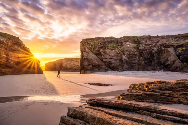 Unrecongisable person walking alone at sunrise in Cathedrals beach (playa de las catedrales), Ribadeo, Galicia, Spain