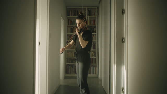 Beautiful young woman musician playing the violin in corridor