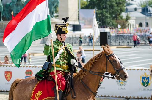 Budapest, Hungary - September 19, 2015: Man in traditional military uniform riding a horse and carrying the Hungarian flag during the cultural Heritage Days' festival