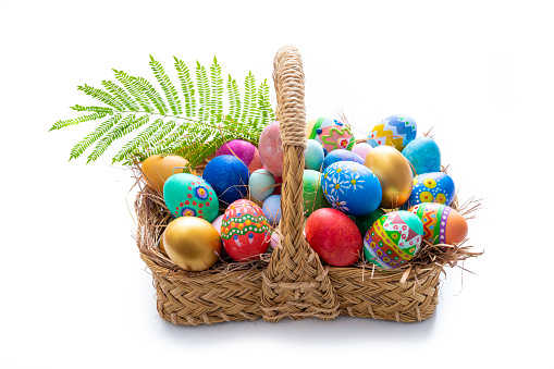 Easter eggs hand painted in a straw basket isolated on white with spring leaves