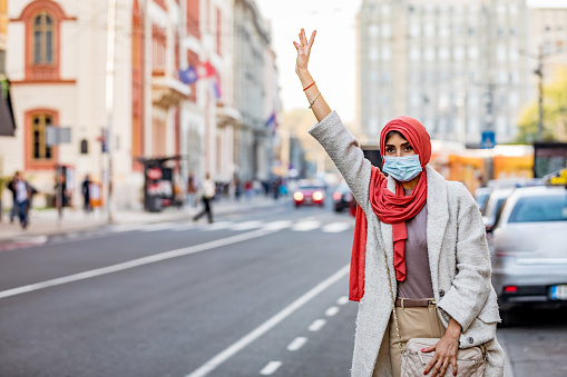 Health protection, safety and pandemic concept - Mature Muslim woman in face protective mask catching taxi on city street