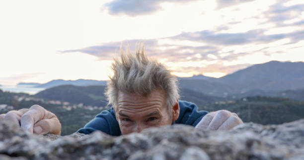 istock Male rock climber reaches for rock summit, with chalked hands 1303545571