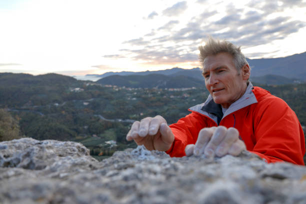 istock Male rock climber reaches for rock summit, with chalked hands 1303546599