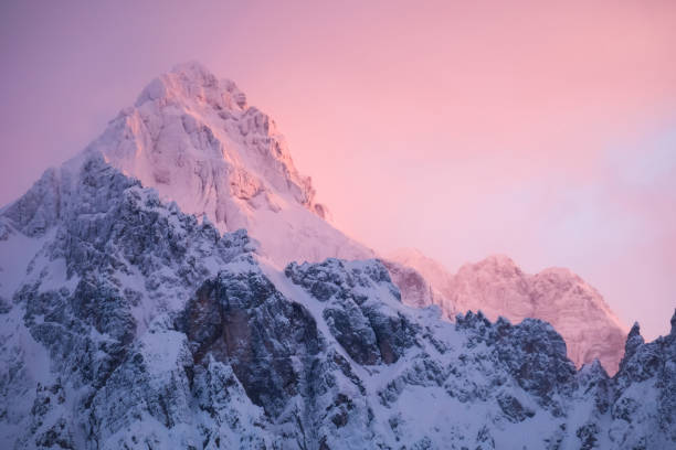 bela foto de perto de um topo rosa brilhante da montanha nos alpes ao pôr do sol enquanto o vento sopra neve fora da montanha. poder dos elementos naturais em um ambiente alpino - alpenglow sunrise sun scenics - fotografias e filmes do acervo