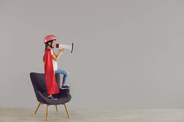 istock A child in a super hero costume shouting in megaphone on a gray background. 1303551211